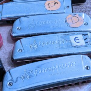 Gros plan sur quatre harmonicas Golden Melody avec des étiquettes de tonalité Ré bémol, Ré et Mi, avec un filtre bleu clair.
