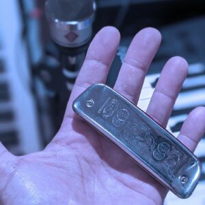  Main gauche tenant un harmonica Golden Melody, microphone Neumann en arrière-plan.